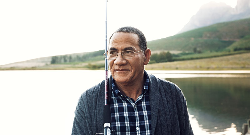 Older man holding a fishing pole on the water.